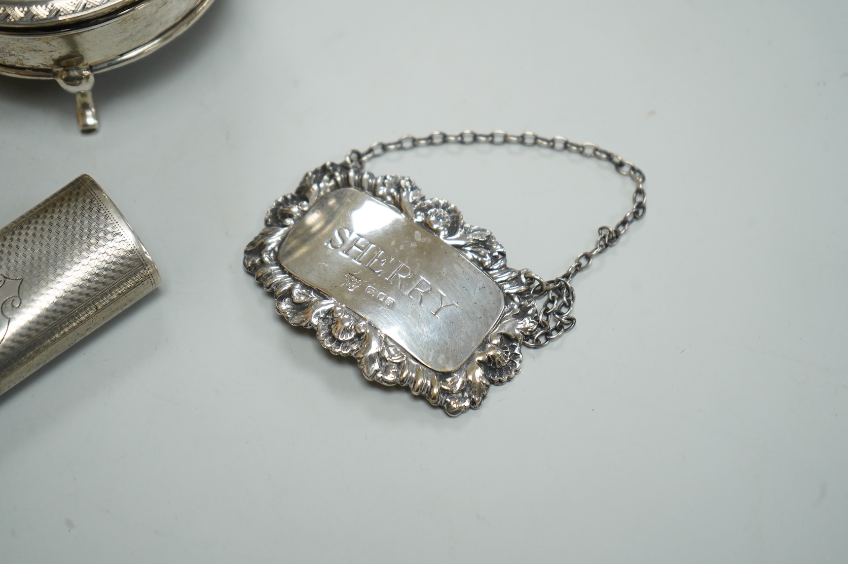 A George V silver mounted circular trinket box by Horton & Allday, Birmingham, 1916, diameter 75mm, together with a 19th century German? white metal vesta case and a modern silver wine label.